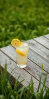 Refreshing lemonade served in a glass with lemon slices on a wooden table surrounded by green grass photo