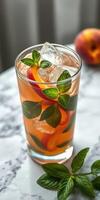 Refreshing herbal peach beverage with ice and mint leaves on a marble surface photo