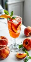 Refreshing peach iced tea served in a clear glass with mint leaves and fresh peaches on a marble countertop photo