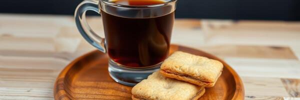 Coffee served in a clear glass with two biscuits on a wooden plate, perfect for an afternoon break photo