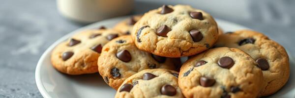 Freshly baked chocolate chip cookies arranged on a white plate with a cup of milk in the background photo