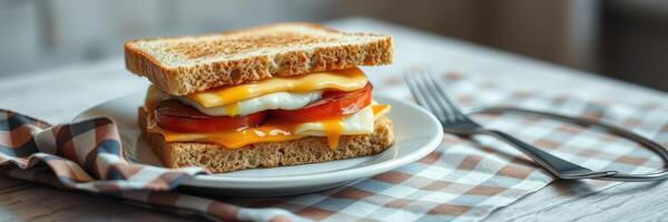 Breakfast sandwich with eggs, cheese, and tomatoes on whole grain bread served on a plate with a fork and napkin photo