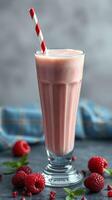 Refreshing raspberry milkshake served in a tall glass with a red striped straw on a textured surface with fresh berries nearby photo
