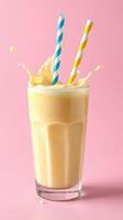 Delicious creamy yellow drink splashes against a vibrant pink background with striped straws photo