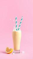 Refreshing citrus smoothie with splashes and colorful straws against a pink background photo