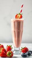 Fresh strawberry smoothie served in a tall glass with a striped straw and mixed berries on the side photo