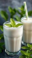 Refreshing mint yogurt drinks served in clear glasses with green leaves in the background during a bright day photo