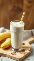Creamy banana smoothie served in a tall glass with a striped straw beside ripe bananas on a wooden cutting board photo