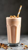 Creamy nut-based smoothie served in a tall glass with a striped straw and topped with crunchy nuts photo