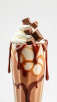 Delicious chocolate shake topped with whipped cream and chocolate chunks served in a clear glass photo