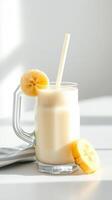 Creamy banana smoothie served in a clear glass with fresh banana slices on the rim in bright sunlight photo