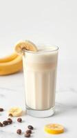 Creamy banana smoothie with coffee and banana slices served in a tall glass on a light countertop photo