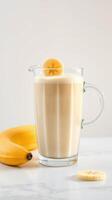 Refreshing banana smoothie served in a clear pitcher alongside fresh bananas on a marble countertop photo
