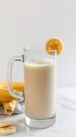 Smooth banana milkshake served in a glass with a banana slice on the rim against a neutral background photo