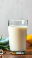 Freshly poured milk in a clear glass on a wooden table with fruits and herbs in the background photo
