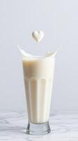 Creamy milkshake splashes in clear glass with heart-shaped drop in the air photo