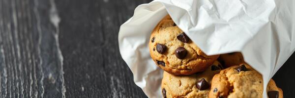 Freshly baked chocolate chip cookies in a brown paper bag on a dark wooden table photo