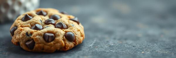 Freshly baked chocolate chip cookie resting on a dark countertop with a blurred background photo