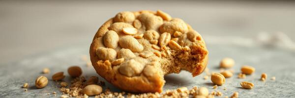 Delicious peanut cookie with a bite taken out, surrounded by scattered nuts on a grey surface photo