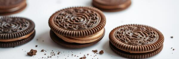 Delicious chocolate cream-filled cookies arranged on a white surface with crumbs scattered around photo
