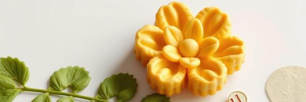 Decorative yellow flower shaped butter rests on a white surface beside green leaves and a round disk at a kitchen workspace photo