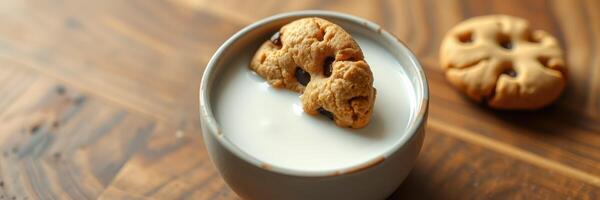 Delicious chocolate chip cookie partially submerged in a bowl of milk on a wooden table photo