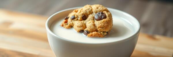 Delicious chocolate chip cookie resting in a bowl of milk on a wooden surface photo