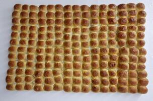 Pav is a soft, slightly sweet, square-shaped bread roll that is a staple in Indian cuisine Rows of bread-like or bun-like objects arranged neatly. They appear golden-brown, likely freshly baked. photo