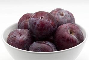 A close-up view of a bowl filled with fresh, ripe plums of varying shades of deep red and purple. photo