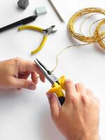 Hands using pliers to trim wire with tools on white surface for diy project photo