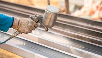 Construction worker painting metal structure surface coating with a spray gun at construction site. Metal corrosion and rust protection. Industrial precision. Protective coating to a metal structure. photo