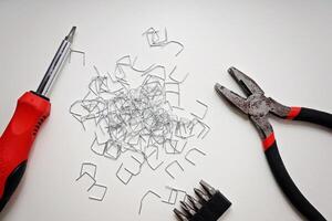 Screwdriver, Pliers, Bits, and Staples Arranged on White Surface with Copy Space. photo
