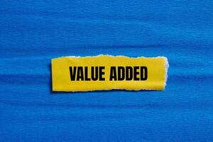 Value added message written on ripped torn yellow paper piece with blue background. Conceptual value added symbol. Copy space. photo