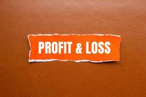 Profit and loss message written on ripped orange torn paper piece with brown background. Conceptual profit and loss symbol. Copy space. photo