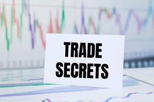 Trade secrets message written on white paper card with financial charts and documents. Conceptual trade secrets symbol. photo