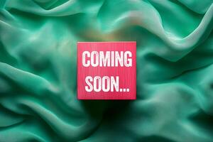 Coming soon message written on pink wooden cube on green fabric background. Conceptual coming soon symbol. Copy space. photo