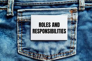Roles and responsibilities message written on white card on denim jean background. Conceptual roles and responsibilities symbol. Copy space. photo