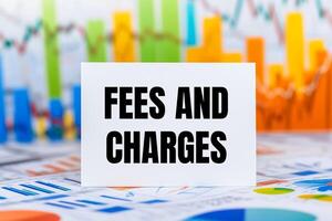 Fees and charges message written on white paper card with financial charts and documents. Conceptual fees and charges symbol. photo