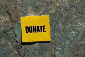 Donate message written on ripped torn yellow paper piece with stone background. Conceptual donate symbol. Copy space. photo