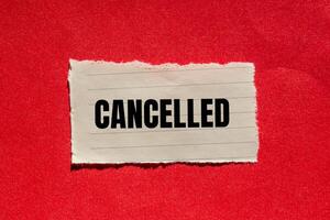 Cancelled message written on ripped torn paper piece with red background. Conceptual cancelled symbol. Copy space. photo