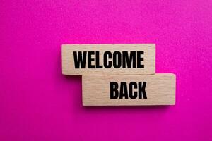 Welcome back message written on wooden blocks with pink background. Conceptual welcome back symbol. Copy space. photo