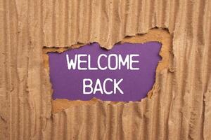 Welcome back message written on ripped torn cardboard paper with purple background. Conceptual welcome back symbol. Copy space. photo