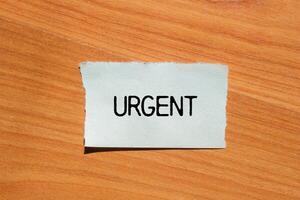 Urgent message written on ripped torn paper piece with wooden background. Conceptual urgent word symbol. Copy space. photo