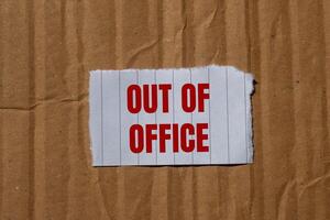 Out of office message written on ripped torn paper piece with cardboard paper background. Conceptual out of office symbol. Copy space. photo