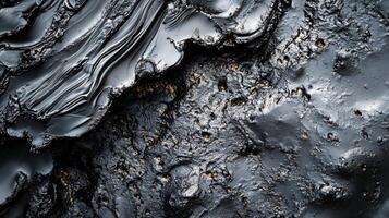 Black and grey image of a rocky surface with a dark liquid on it. The liquid appears to be oil or tar. The image has a moody and ominous feel to it, as if it is a warning of the dangers of pollution photo