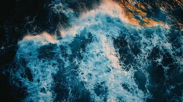 The ocean is rough and choppy, with waves crashing against the shore. The water is a deep blue color, and the sky is a dark blue. Scene is one of power and energy photo