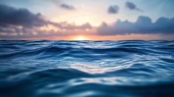 The ocean is calm and the sun is setting. The water is a deep blue color. The sky is a mix of blue and orange photo