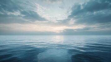 The ocean is calm and the sky is cloudy. The sun is setting, casting a warm glow over the water photo