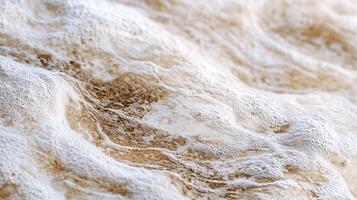 The image is of a wave with a lot of white foam and sand. The foam and sand are scattered all over the wave, giving it a rough and chaotic appearance. Scene is one of turbulence and unpredictability photo