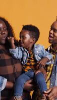 vertical africano americano mãe e Papai ensino seus filho quão para cantar dentro estúdio, Aprendendo para executar canções em microfone a partir de uma jovem idade. adorável pequeno Garoto cantando uma Novo melodia. Câmera b. video